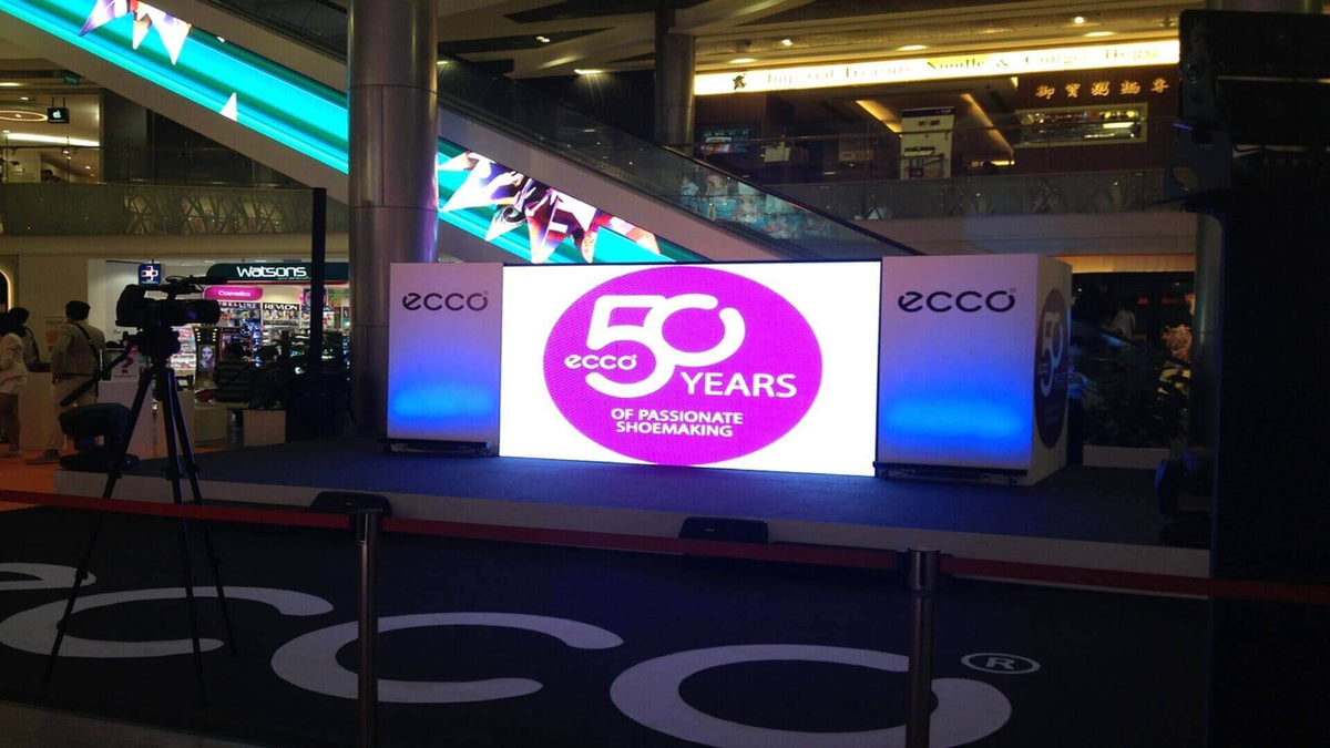 A product launch stage in a shopping mall atrium with an LED screen, lit side panels and a video camera on a tripod.