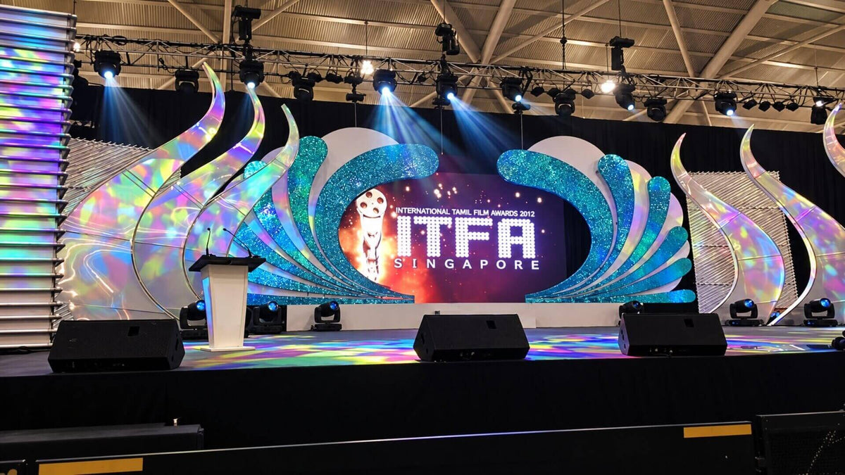 An awards stage with a sculpted set, a central LED screen, moving-head lights on overhead truss and stage monitors along the front edge.