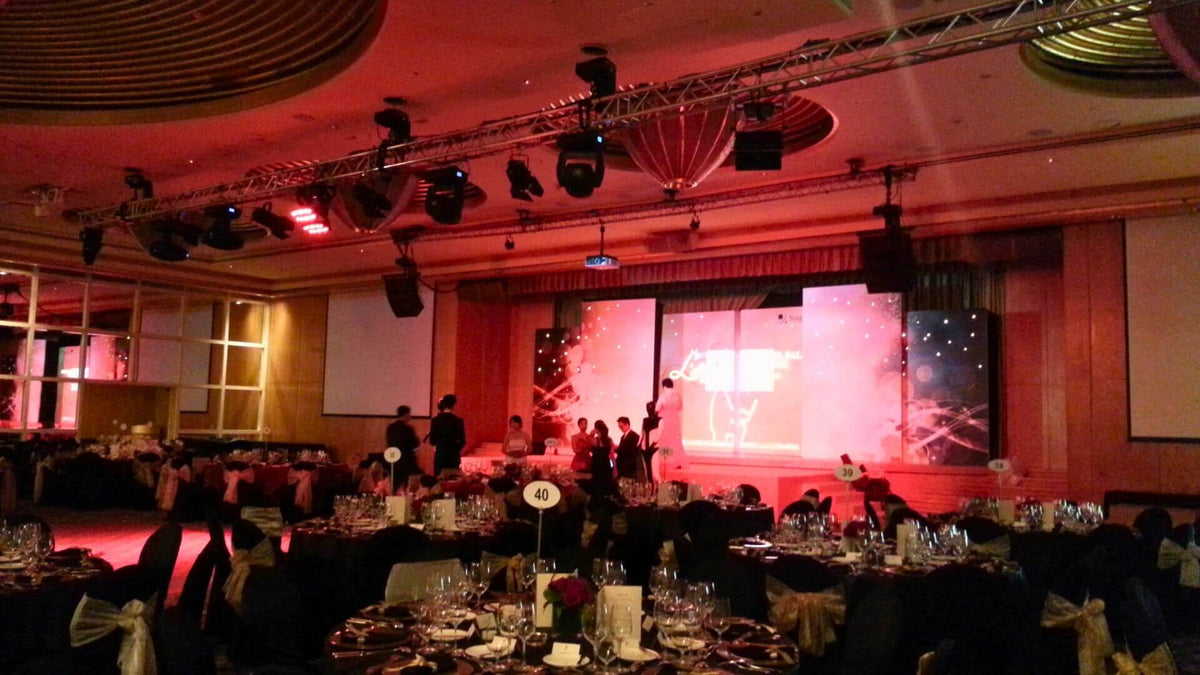 A ballroom lit in red, with event lighting on overhead truss above banquet tables.